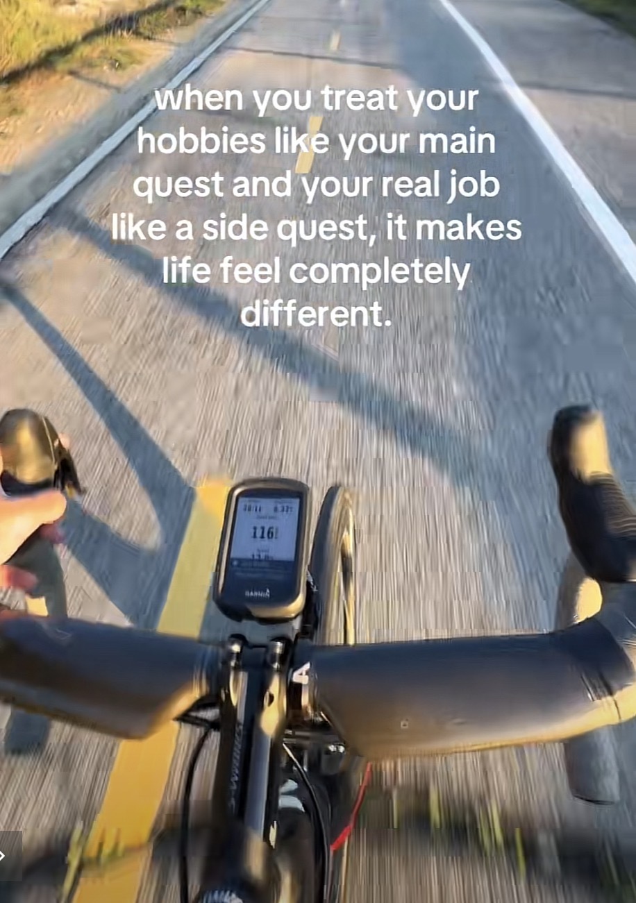 POV of a cyclist riding on a road with the caption “when you treat your hobbies like your main quest and your real job like a side quest, it makes life feel completely different.”