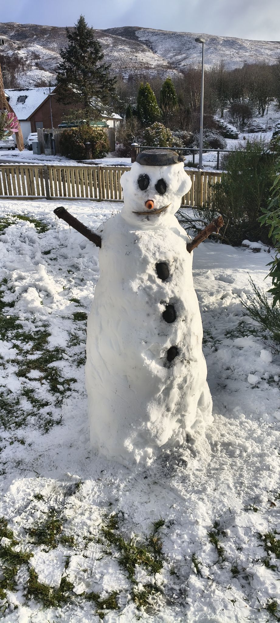 snowman in a garden with snowcapped hills in the background